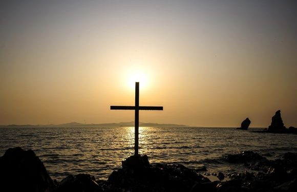 Cross near the sea with sun behind